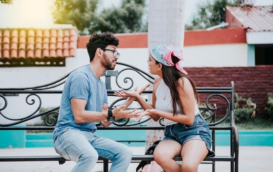 Man arguing with his girlfriend sitting in a park. Young couple arguing sitting on a park bench, Concept of aggressive couples in the park. Upset couple arguing on a park bench