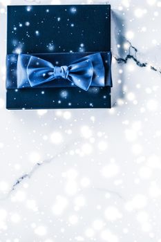 Branding, glamour and cold season concept - Winter holiday gift box with blue silk bow, snow glitter on marble background as Christmas and New Years presents for luxury beauty brand, flatlay design