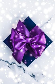 Branding, glamour and cold season concept - Winter holiday gift box with purple silk bow, snow glitter on marble background as Christmas and New Years presents for luxury beauty brand, flatlay design