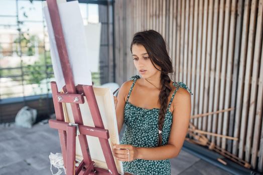 Beautiful woman artist drawing her picture on canvas with oil colors in studio