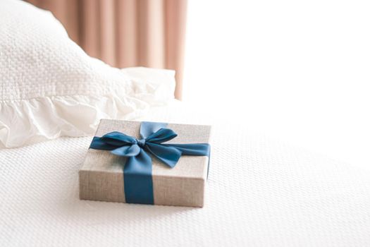 Holiday present and luxury online shopping delivery, wrapped linen gift box with blue ribbon on bed in bedroom, chic countryside style, close-up