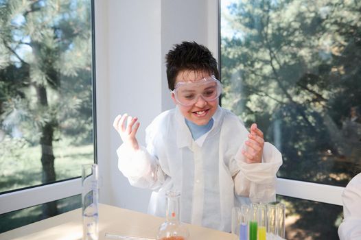 Mischievous teenage boy in safety eyewear and lab coat, fascinated by scientific experiments in chemistry laboratory. Concept of Back to school. Open to new knowledges on of the academic year semester