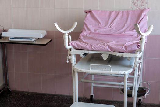 Image of old pink gynecological chair in toffice room professional clinic with copy space. Pregnancy Planning parturition lying-in maternity pain obstetrics Concept.