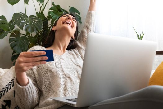 Euphoric and excited woman with arms up shopping online at home using laptop and credit card. Copy space. Online shopping.
