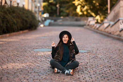 Young woman sitting at city show finger up, new idea, warm autumn day