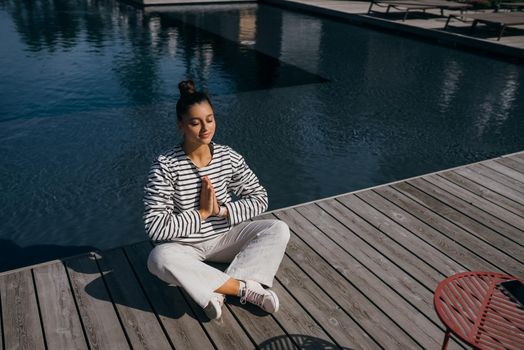 Young fitness woman doing her morning yoga routine at the open air near the pool