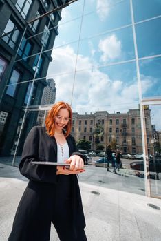 A young woman walks down the street with a laptop by the modern building