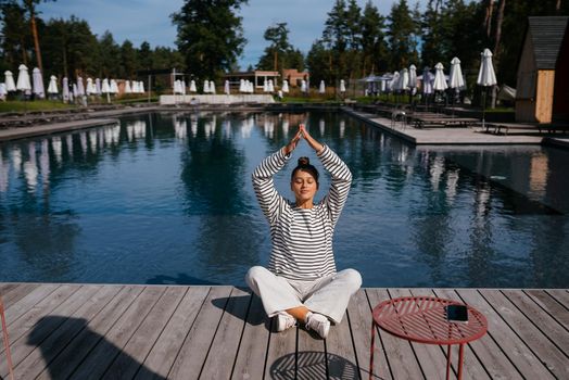 Young fitness woman doing her morning yoga routine at the open air near the pool