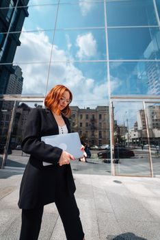 A young woman walks down the street with a laptop by the modern building