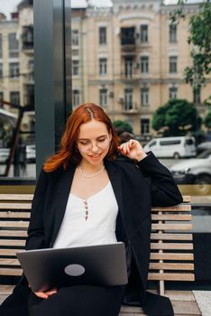 Beautiful redhead woman working on laptop at outdoors cafe