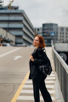 Young beautiful smiling happy woman with backpack poses on a camera while standing on the road