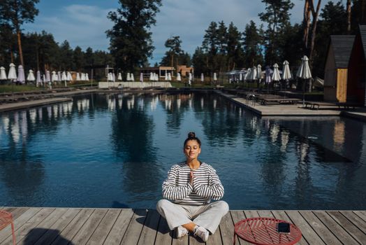 Young fitness woman doing her morning yoga routine at the open air near the pool