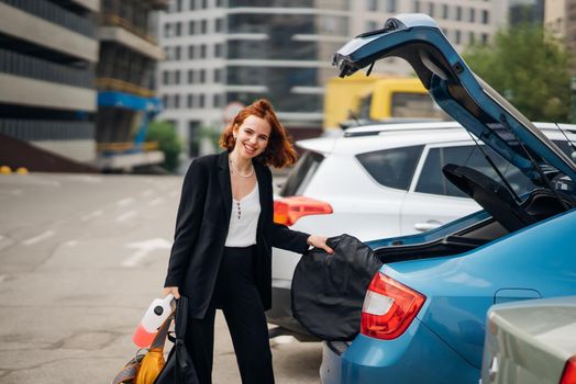 A young woman is packing luggage into the car trunk