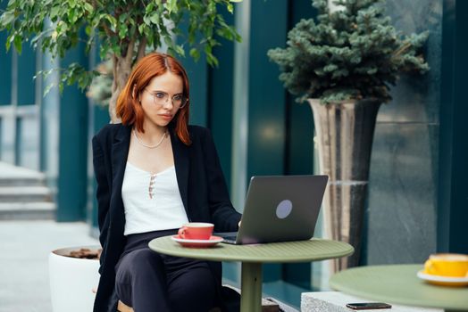 Beautiful redhead woman working on laptop at outdoors cafe