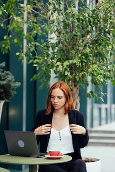 Beautiful redhead woman working on laptop at outdoors cafe