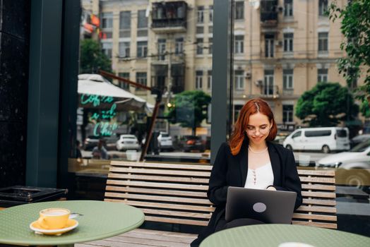 Beautiful redhead woman working on laptop at outdoors cafe