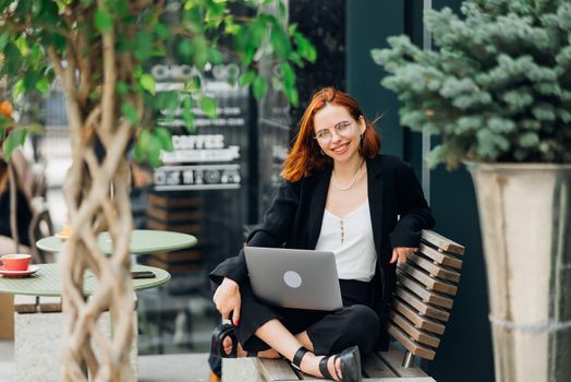 Beautiful redhead woman working on laptop at outdoors cafe
