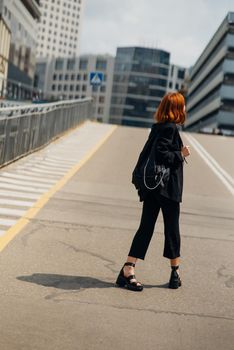 Young beautiful smiling happy woman with backpack poses on a camera while standing on the road