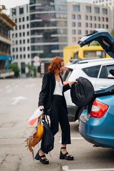 A young woman is packing luggage into the car trunk