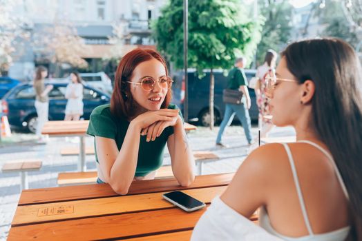 Two pretty girlfriends talking while sitting in a bar at the city street