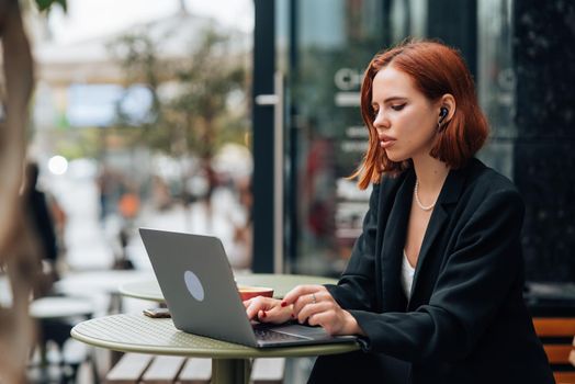 Beautiful redhead woman working on laptop at outdoors cafe