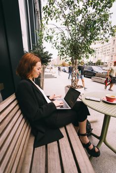 Beautiful redhead woman working on laptop at outdoors cafe