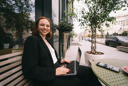 Beautiful redhead woman working on laptop at outdoors cafe