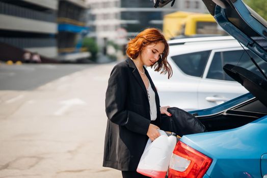 A young woman is packing luggage into the car trunk