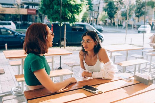 Two pretty girlfriends talking while sitting in a bar at the city street