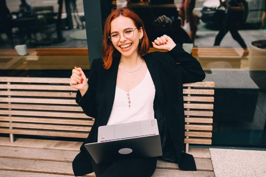 Beautiful redhead woman working on laptop at outdoors cafe