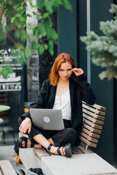 Beautiful redhead woman working on laptop at outdoors cafe