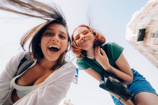 Two funny friends looks down outdoors in the street at camera in the sky background