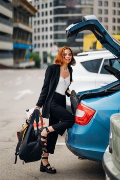 A young woman is packing luggage into the car trunk