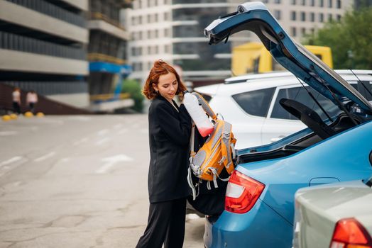 A young woman is packing luggage into the car trunk