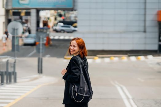 Young beautiful smiling happy woman with backpack poses on a camera while standing on the road