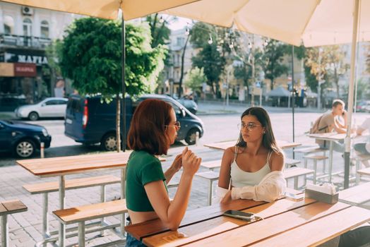 Two pretty girlfriends talking while sitting in a bar at the city street