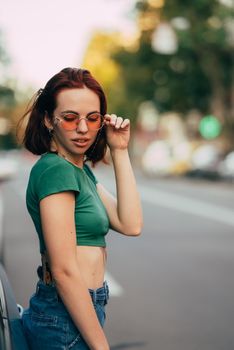 Young woman in glasses posing near car