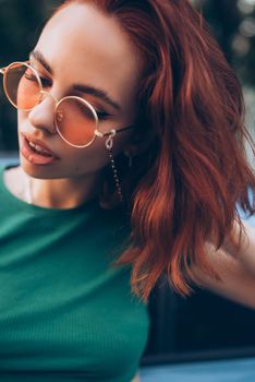 Young woman in glasses posing near car