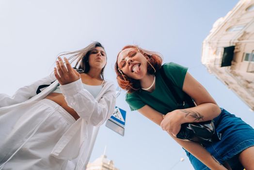 Two funny friends looks down outdoors in the street at camera in the sky background