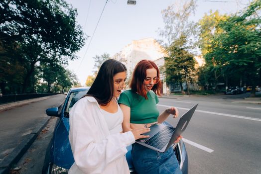 Two young women with a laptop near the car on the road