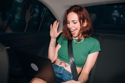 Beautiful woman is using a laptop and smiling while sitting on back seat in the car