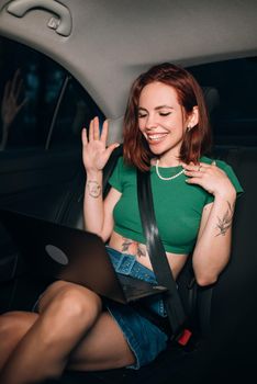 Beautiful woman is using a laptop and smiling while sitting on back seat in the car