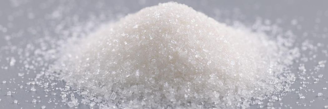 Close-up of pile of sugar crystals on grey surface, focus on heap of sweet powder to add in dishes. Ingredient, cooking, food, sugar substitute concept