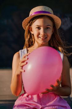 Portrait of a girl in a hat with a pink balloon. She is dressed in pink clothes and her hair is long and loose