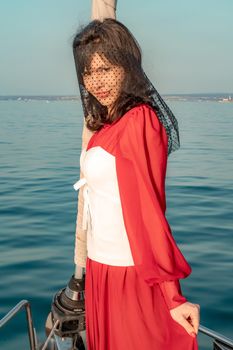 Attractive middle-aged woman in a red dress on a yacht on a summer day. Luxury summer adventure, outdoor activities