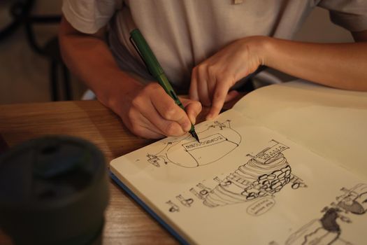 The girl draws with a fountain pen in a sketchbook. Green fountain pen in a woman's hand. Notepad for sketches and notes. Sketching in a cafe. Doodle. Creation.