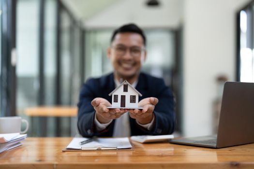 Close up view of young man holding house model. Property insurance and real estate concept