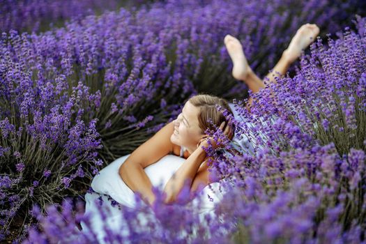 A middle-aged woman lies in a lavender field and enjoys aromatherapy. Aromatherapy concept, lavender oil, photo session in lavender.