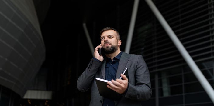 real estate agent speaks on a mobile phone with a notepad in his hands on the background of the office center.