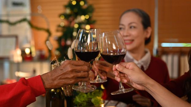 Family toasting wine at Christmas dinner, focus on hands and wine glasses. Holidays and celebration concept.